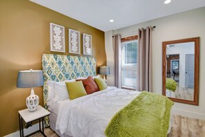 A hotel room with a bed, a nightstand, a lamp, a mirror, and a window with curtains. - Comfy 1 Bedroom Apartment! Salt Lake City. Close to UofU (Salt Lake City)