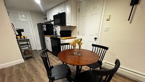 A dining area with a round wooden table, four black chairs, and a vase with dried flowers.