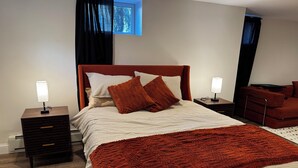 A neatly arranged bedroom with a bed, two bedside tables, a nightstand, and a window with curtains.