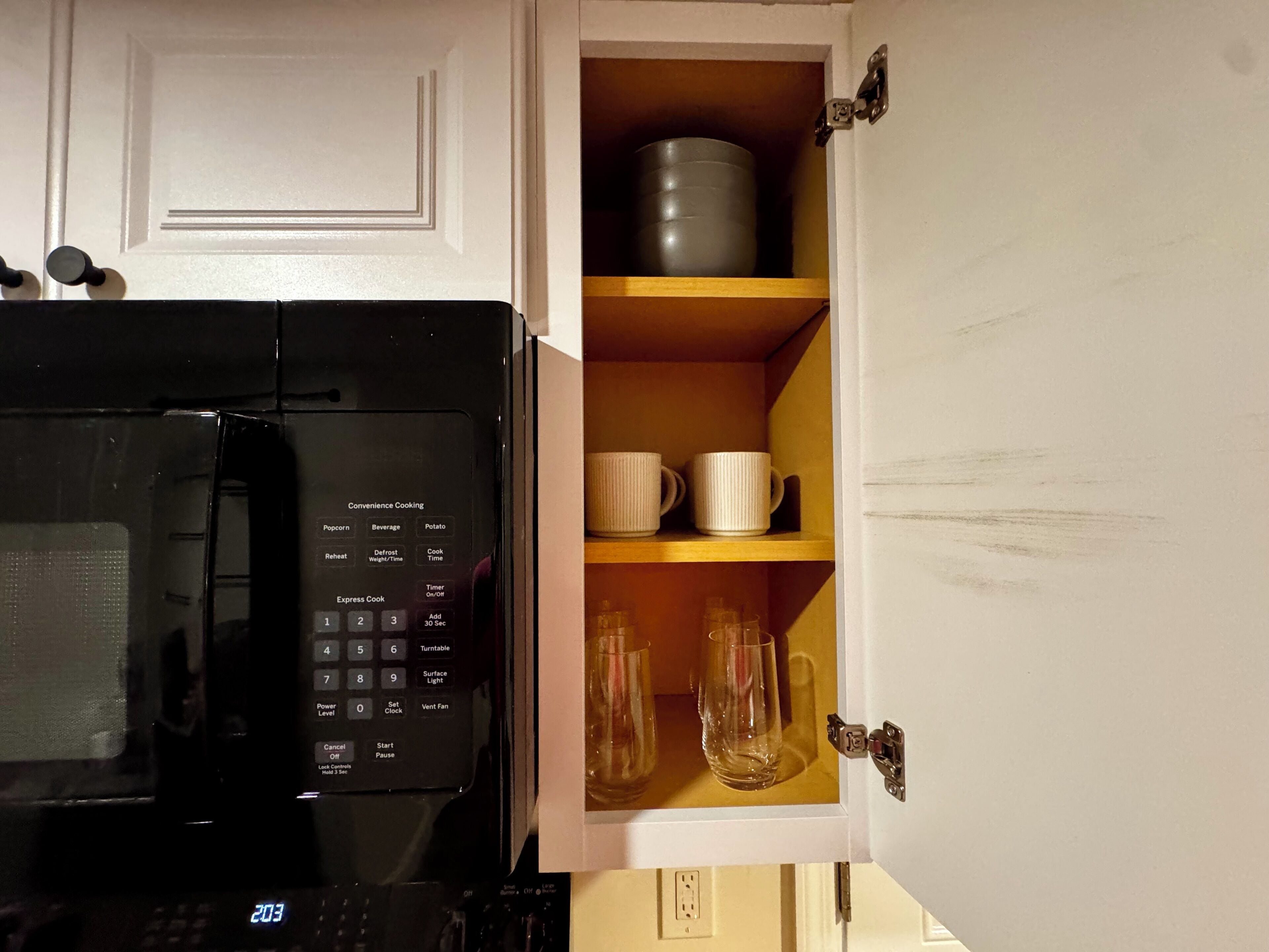 Une cuisine équipée d’un four à micro-ondes et d’un placard contenant des tasses et des verres.