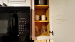 A kitchen with a microwave and a cabinet containing mugs and glasses.