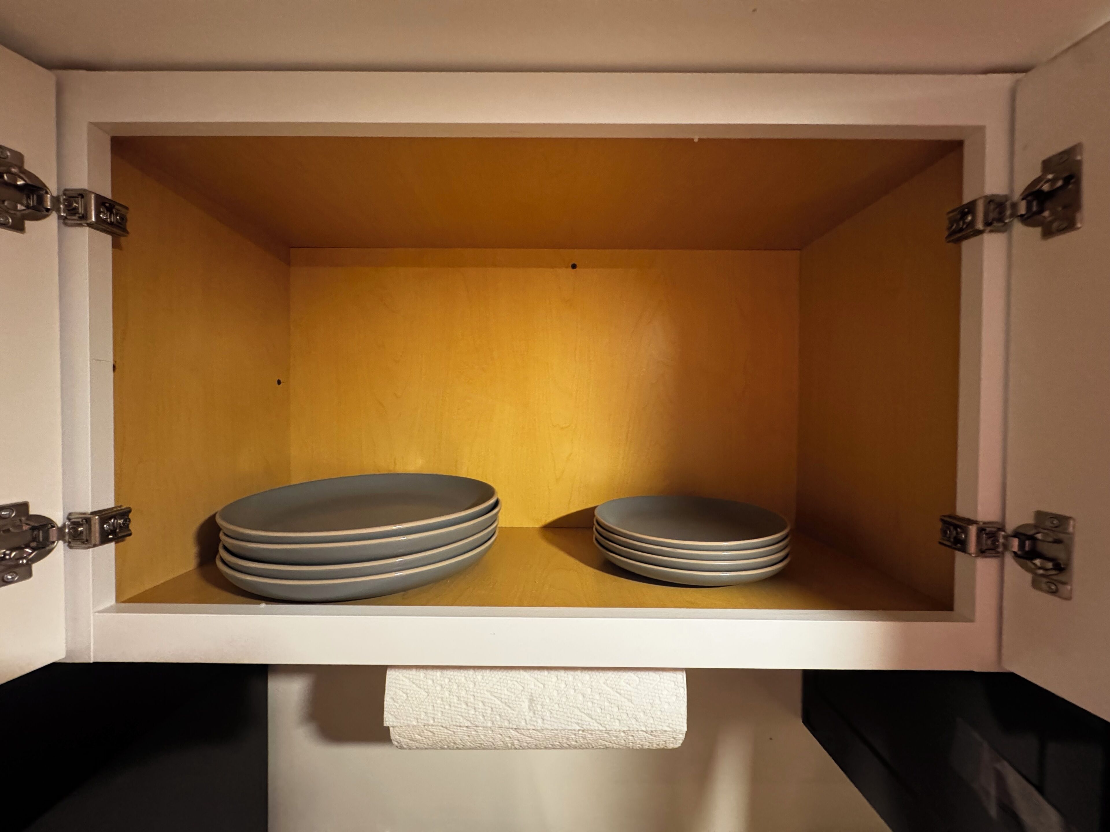 Un meuble de rangement dont l’intérieur est blanc, contenant une pile d’assiettes et un rouleau d’essuie-tout.