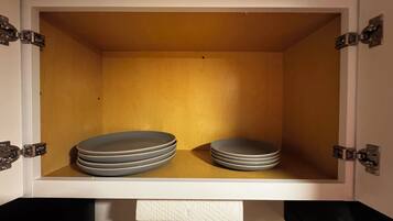 Un meuble de rangement dont l’intérieur est blanc, contenant une pile d’assiettes et un rouleau d’essuie-tout.