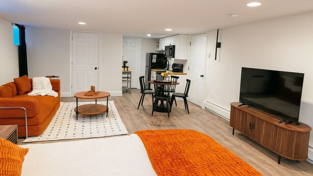 A modern living room with a sofa, a coffee table, a TV, and a dining area with chairs and a table.