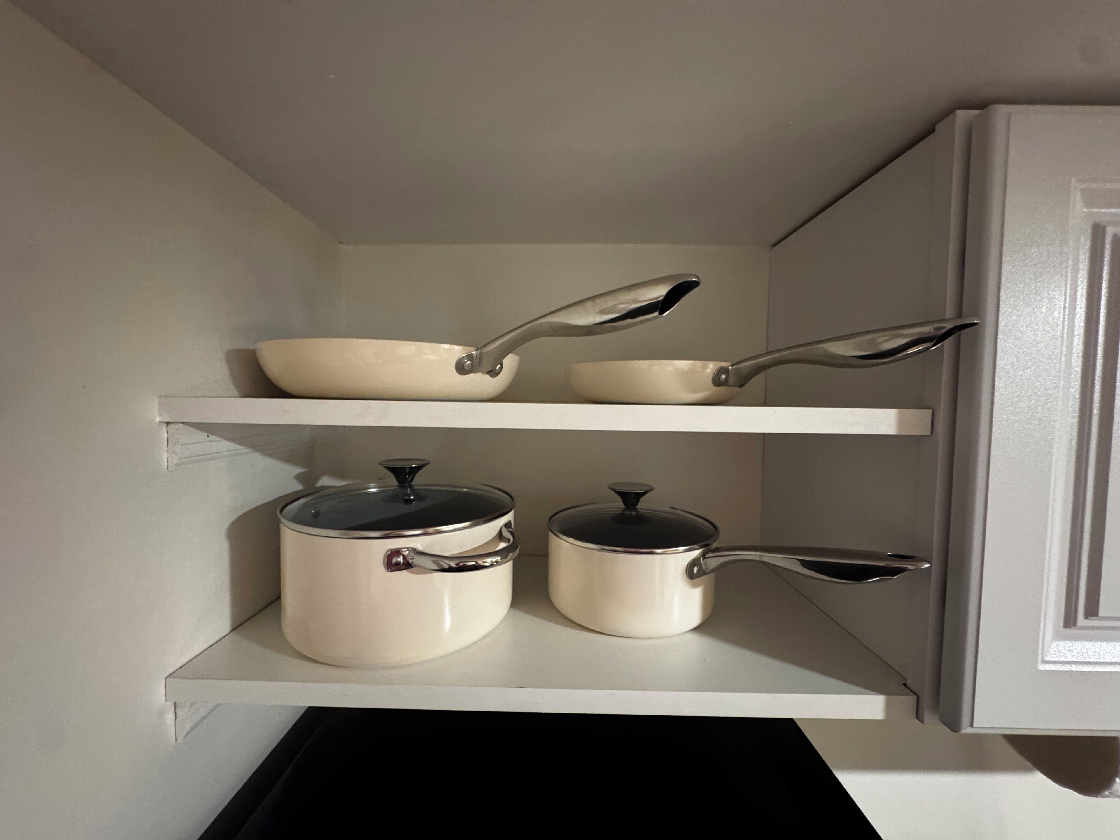 Un garde-manger de cuisine avec des armoires et des étagères blanches, contenant des ustensiles de cuisine et des casseroles.