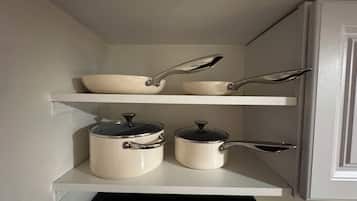 Un garde-manger de cuisine avec des armoires et des étagères blanches, contenant des ustensiles de cuisine et des casseroles.