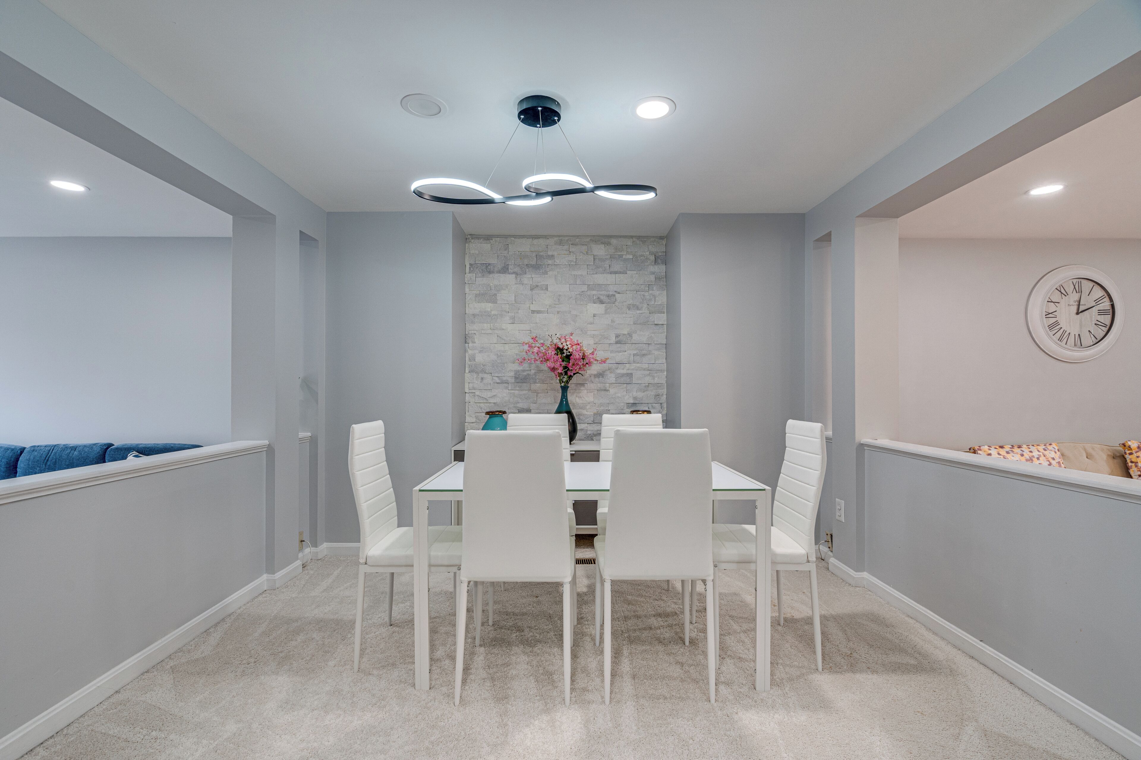 Un coin repas avec une table blanche, des chaises et une horloge au mur.