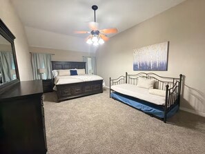 Un dormitorio con cama, cómoda, ventilador de techo y un cuadro en la pared.