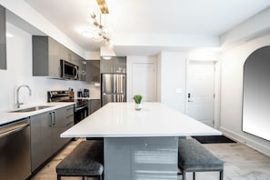 Cozinha moderna com eletrodomésticos de aço inoxidável, uma ilha branca com assentos e design minimalista.