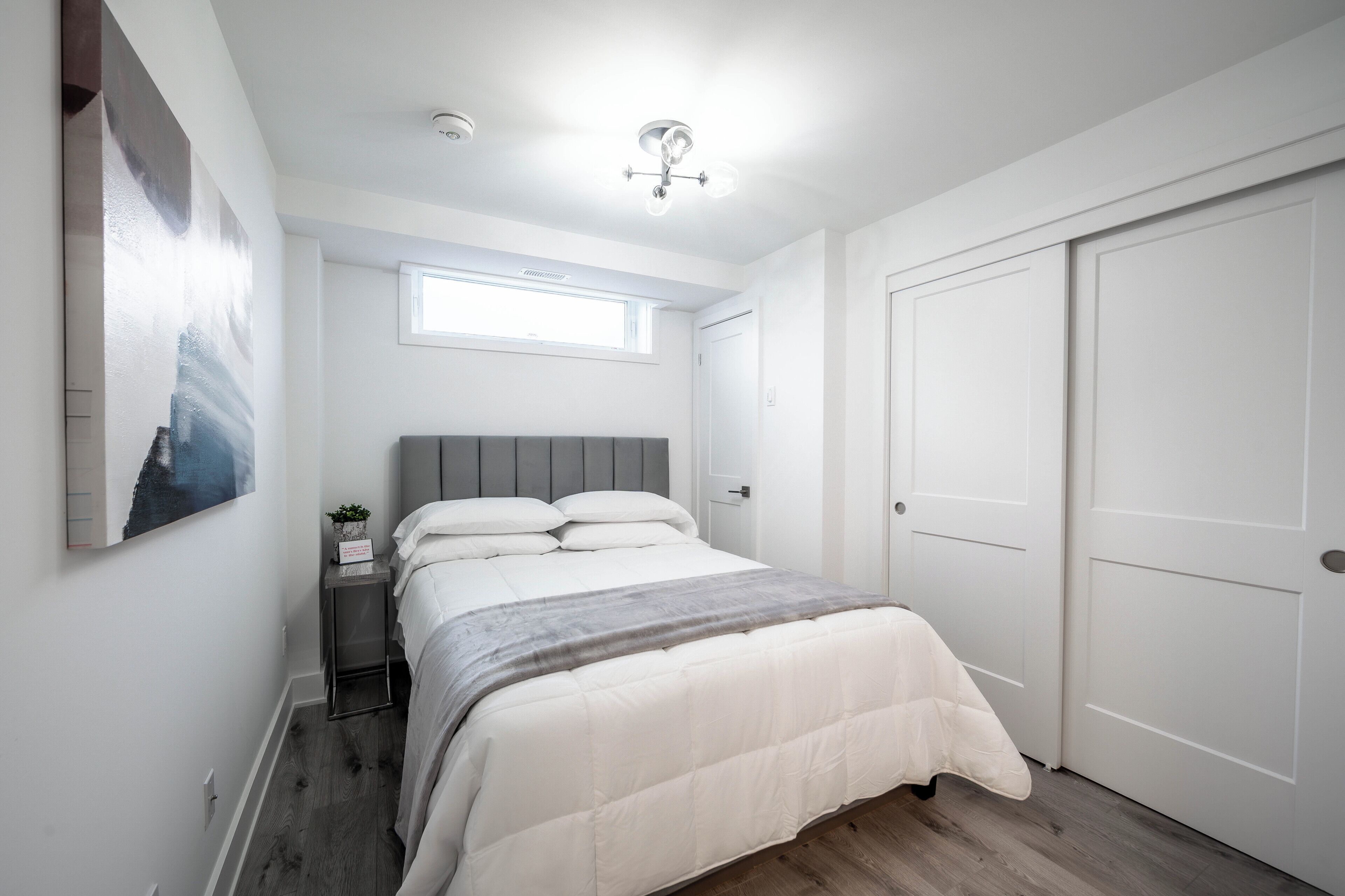 A bedroom with a bed, a nightstand, a window, and a door.