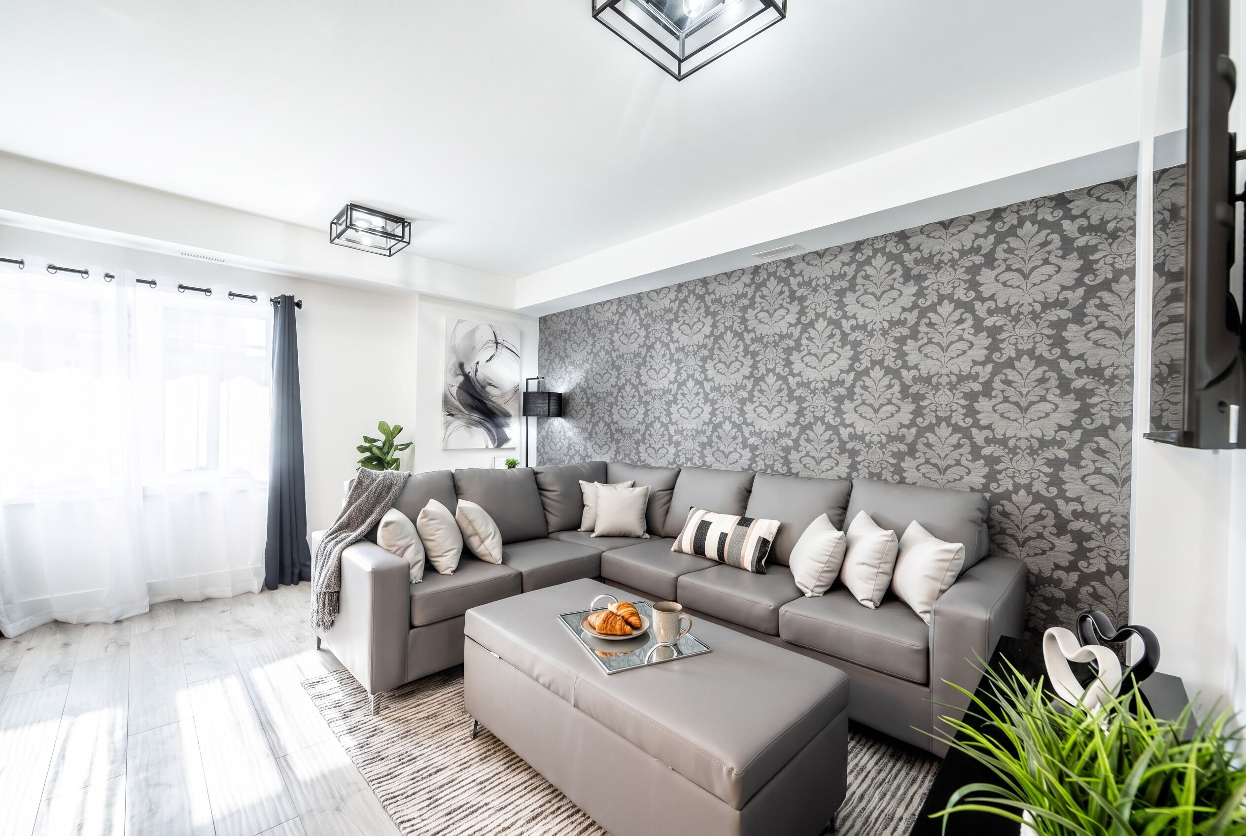 A modern living room with a grey sectional sofa, a coffee table, and a patterned wallpaper.