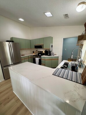 A modern kitchen with a central island, stainless steel appliances, and green cabinetry.