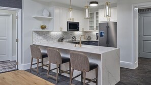 A modern kitchen with a central island, bar stools, stainless steel appliances, and pendant lighting.