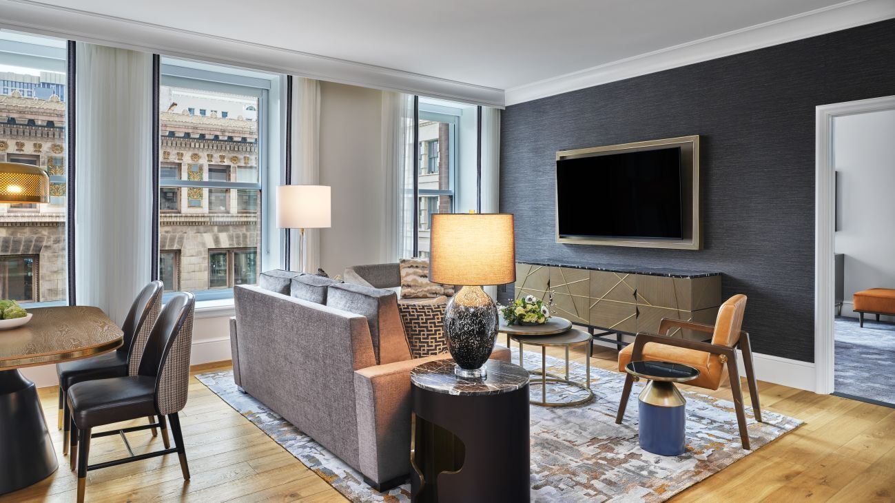 Une chambre d’hôtel moderne équipée d’un canapé, de fauteuils, d’une table à manger et d’un téléviseur fixé au mur.