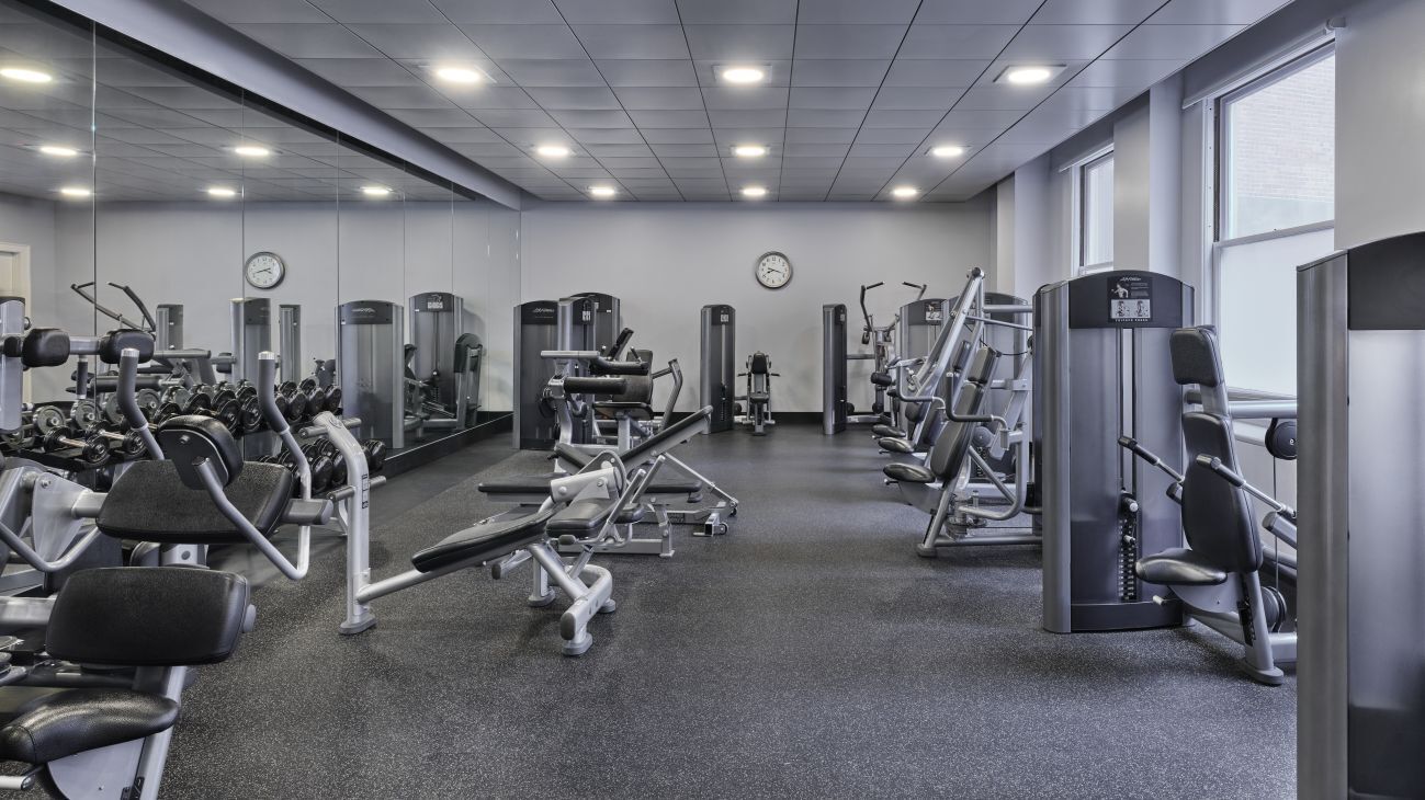 A gym with various exercise machines, mirrors, and a clock on the wall.