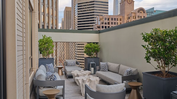 A modern outdoor seating area with sofas and chairs, potted plants, and a decorative wall.