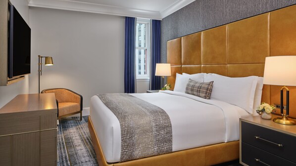A hotel room with a bed, bedside tables, a desk, a chair, and a television.