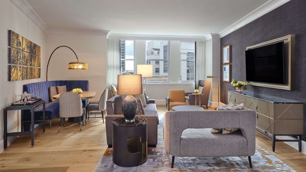A modern living room with a sofa, armchairs, a coffee table, and a TV mounted on the wall.
