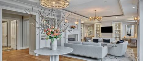 A modern living room with a grey sofa, a round table with a vase of flowers, and a chandelier.