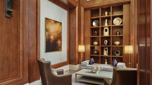 A room with a wooden paneled wall, a large abstract painting, a sofa, a coffee table with flowers, and a shelf with decorative items.