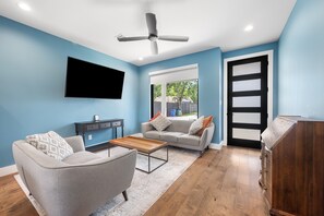 A living room with a flat-screen TV, a ceiling fan, a sofa, a coffee table, and a wooden cabinet. - Central Austin Cozy Retreat, 3 Bedroom, 2.5 bath, Large Outdoor Pool & Spa (Austin)