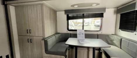 A compact interior with a table and bench seating, a window with blinds, and a door with a handle.