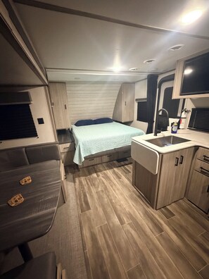 Ein kompaktes Wohnmobil-Interieur mit Bett, Küchenzeile und Sitzgelegenheit.