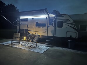 Ein gut beleuchteter Wohnmobil mit dem Schriftzug 'Passport', ein kleiner Tisch mit Lampe, zwei Stühle und ein Betonboden.