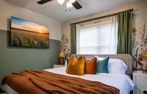 A bedroom with a bed, a nightstand, a lamp, a painting, and a window with curtains. - New Wildflower Lodge and Espresso/Cappuccino/Karaoke Cafe-EXPO-TU-KING-Sleeps 8 (Tulsa)