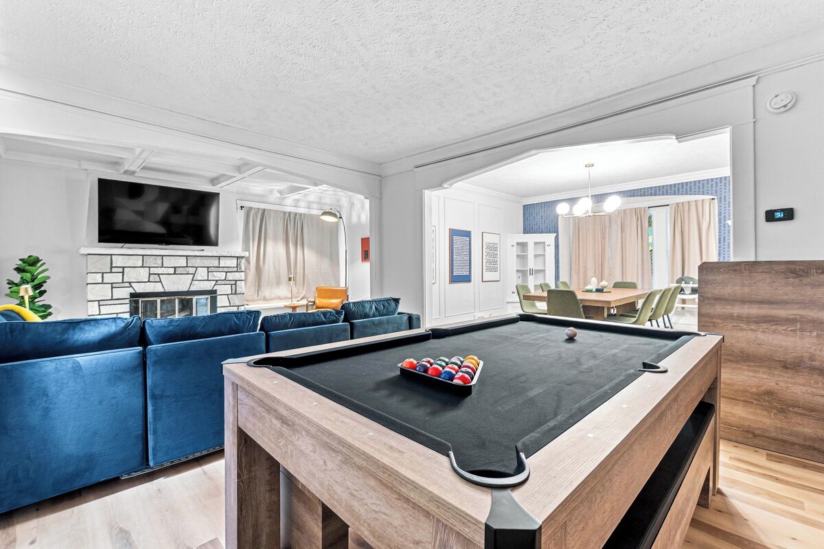 Une table de billard avec un jeu de billard (queue et billes), un canapé bleu et un téléviseur fixé au mur.