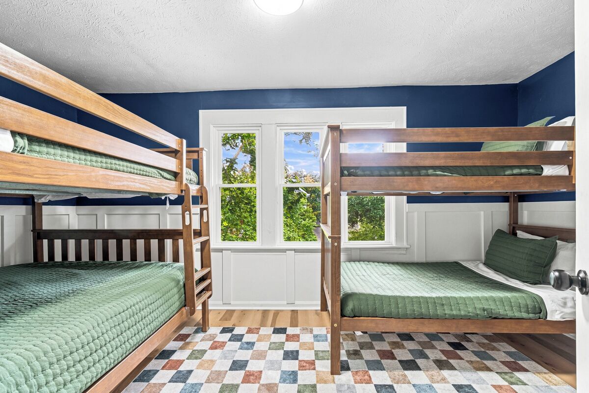 A room with bunk beds, a checkered floor, and a window with a view of trees.