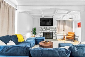 Ein modernes Wohnzimmer mit Kamin aus Stein, blauen Sofas, einem runden Couchtisch und einem Fernseher, der über dem Kamin angebracht ist.