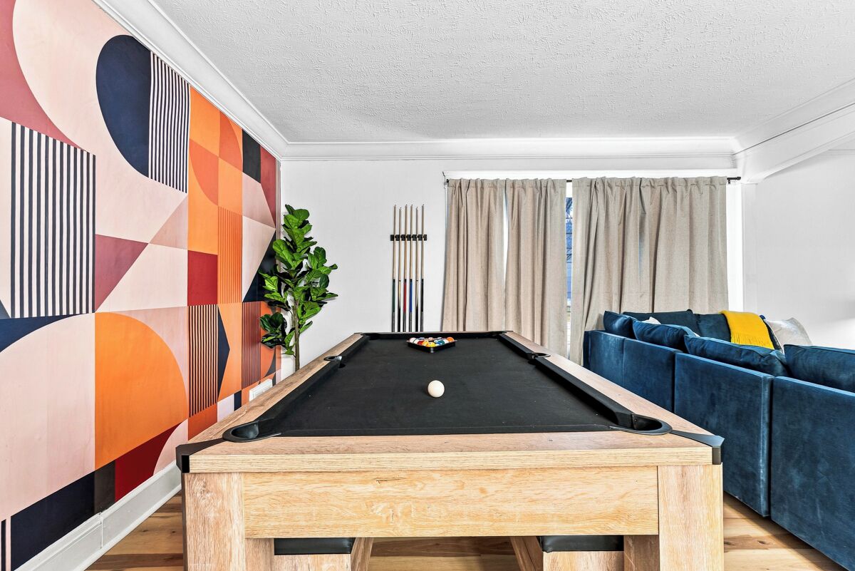 A pool table in a room with a geometric-patterned wall, a sofa, and a plant.
