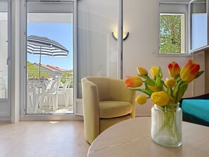 A room with a sliding glass door leading to an outdoor seating area, a round table with a vase of flowers, and a sofa. - Le Hameau du Golf by Interhome (Pornic)