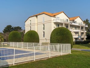 A two-story building with a swimming pool, surrounded by a white fence, and three well-maintained spherical hedges. - Le Hameau du Golf by Interhome (Pornic)