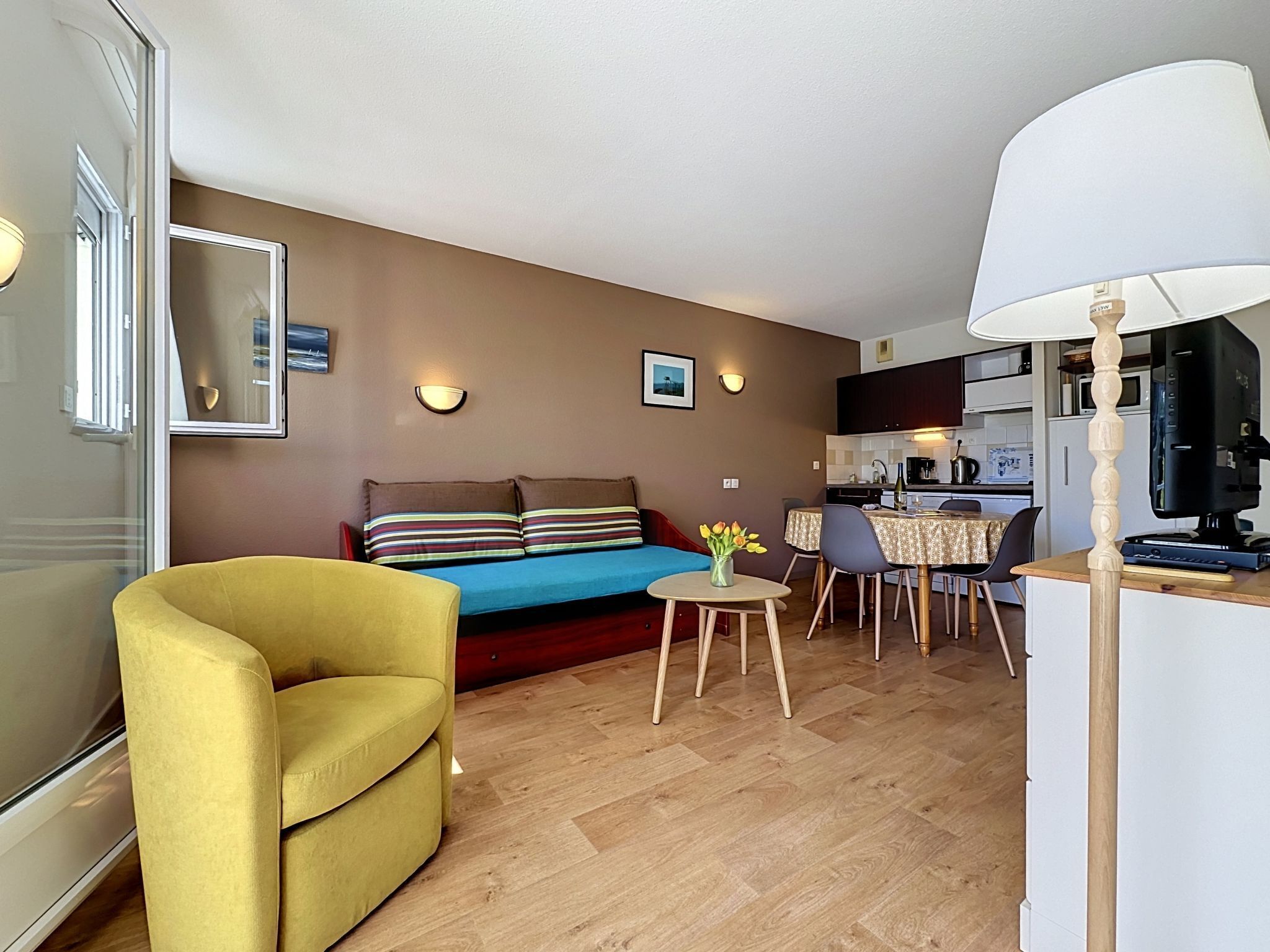 Un espacio habitable compacto con sofá, un sillón amarillo, una mesa de comedor y una kitchenette.