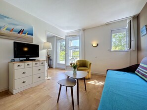 A modern living room with a flat-screen TV, a sofa, a small table with a vase of flowers, and a chair. - Le Hameau du Golf by Interhome (Pornic)