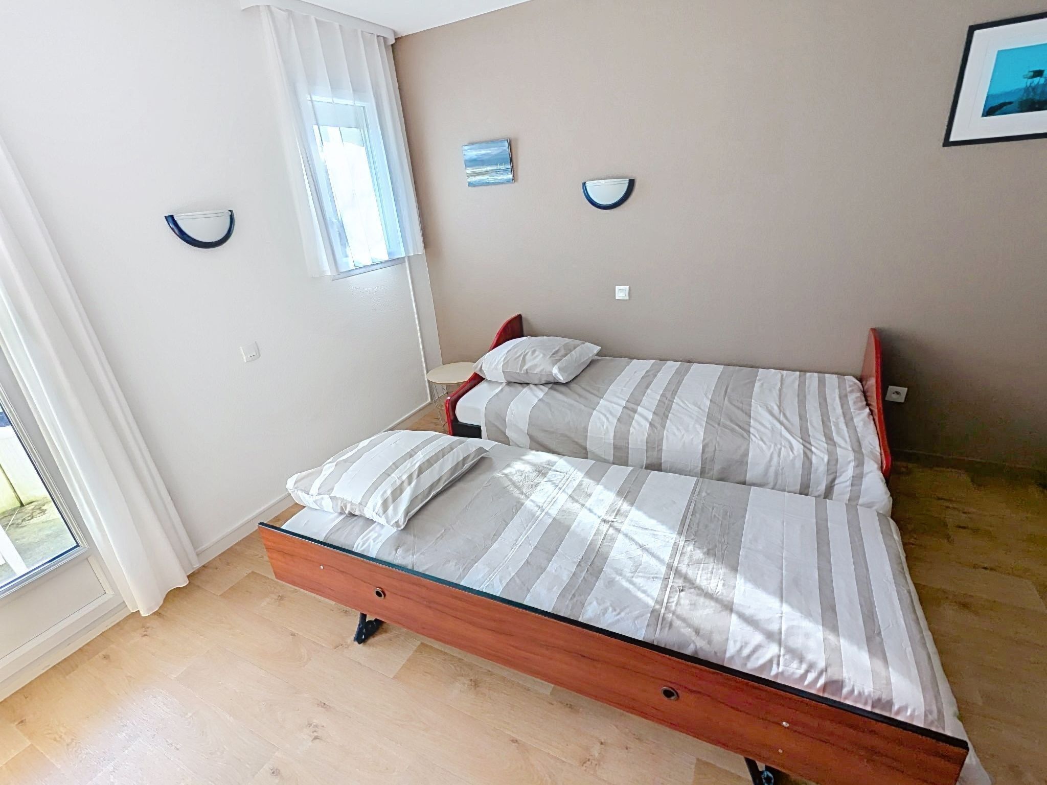 A bedroom with a bed, two pillows, a bedside table, a window with curtains, and a wall-mounted light fixture.