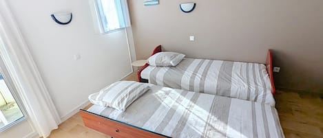 Un dormitori amb llit, dos coixins, una taula de nit, una finestra amb cortines i una làmpada de paret.