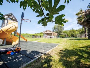 Un parc infantil amb tobogan i cèrcol de bàsquet, zona de pícnic coberta i jardí tancat.