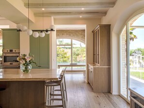 A modern kitchen with a large island, bar stools, a built-in oven, and a view of the outdoors. - Tenuta Marino – con piscina privata by Interhome (Cesano)