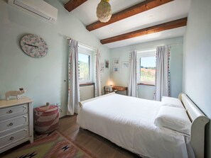 Un dormitori amb llit, calaixera, radiador i finestra amb cortines.