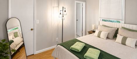 A bedroom with a bed, bedside table, lamp, and a mirror.