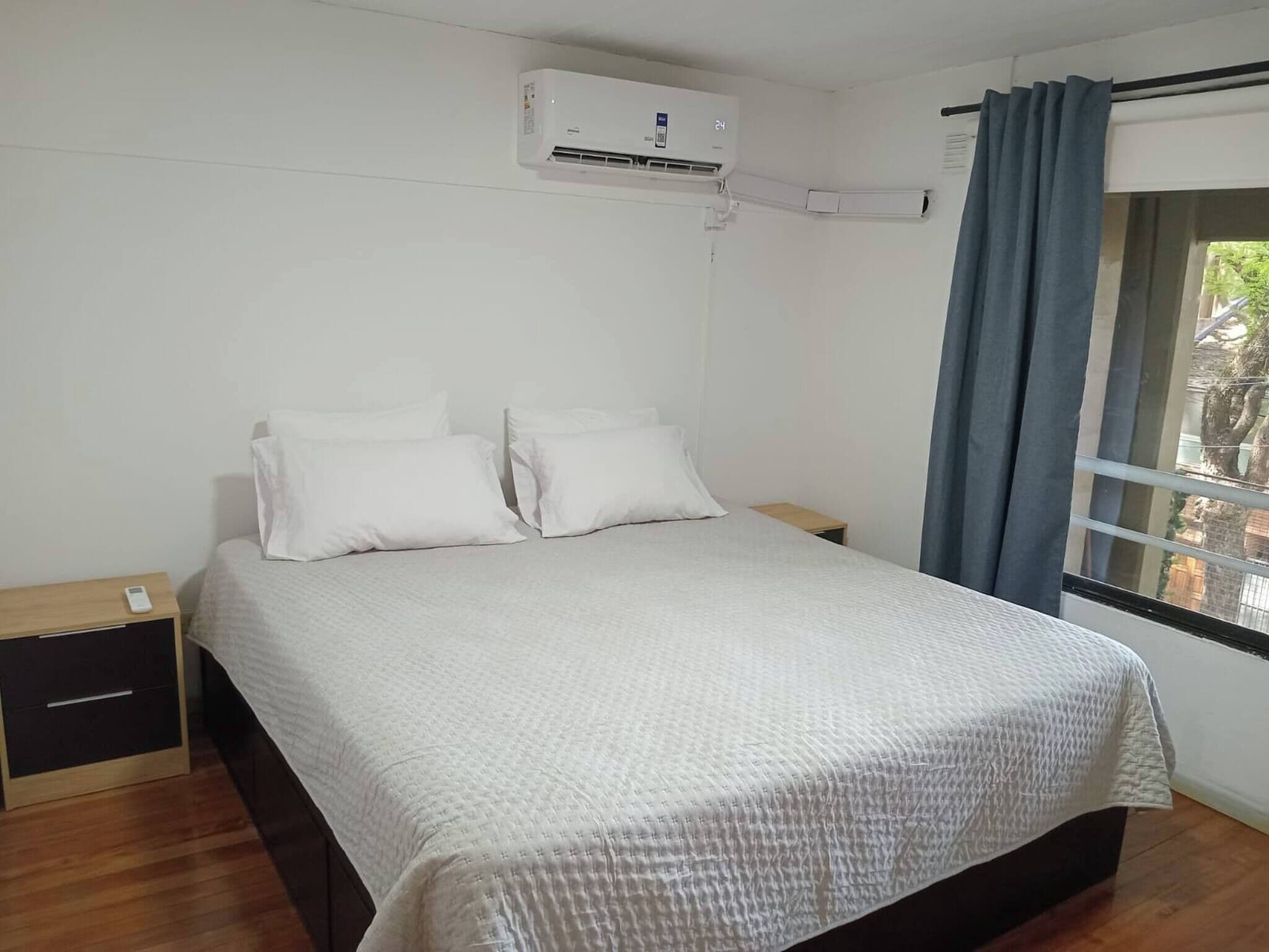 Una camera da letto con un letto, un comodino, un condizionatore d'aria a parete e una finestra con tende.