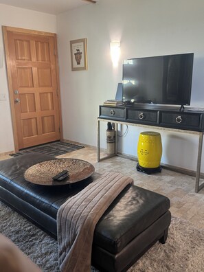 Ein Wohnzimmer mit einem schwarzen Ledersofa, einem Fernseher auf einem Schrank, einem gelben Blumenvasen und einer Holztür.