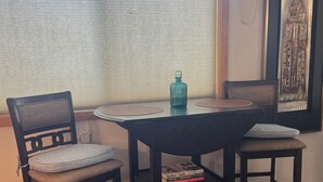 En matplats med ett bord och två stolar, en blå flaska och en inramad tavla på väggen.