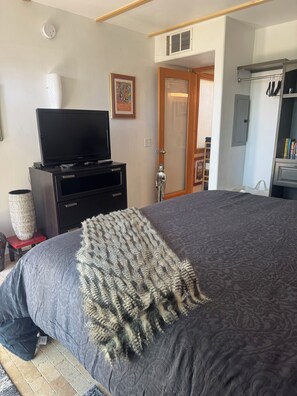 A bedroom with a bed, a television on a dresser, a Buddha statue, and a door leading to another room. - Palm Desert Retreat with Pool-Furnished 30+ Day Stay (Desert Hot Springs)