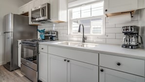 A modern kitchen with white cabinets, stainless steel appliances, a double sink, and a window above the sink. - 66 Cottage on Historic Rt 66 -Starlit Stone (El Reno)