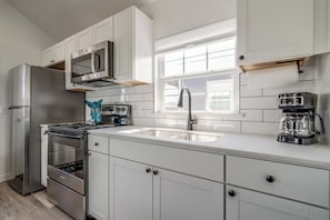 A modern kitchen with white cabinets, stainless steel appliances, a double sink, and a window above the sink. - 66 Cottage on Historic Rt 66 -Starlit Stone (El Reno)