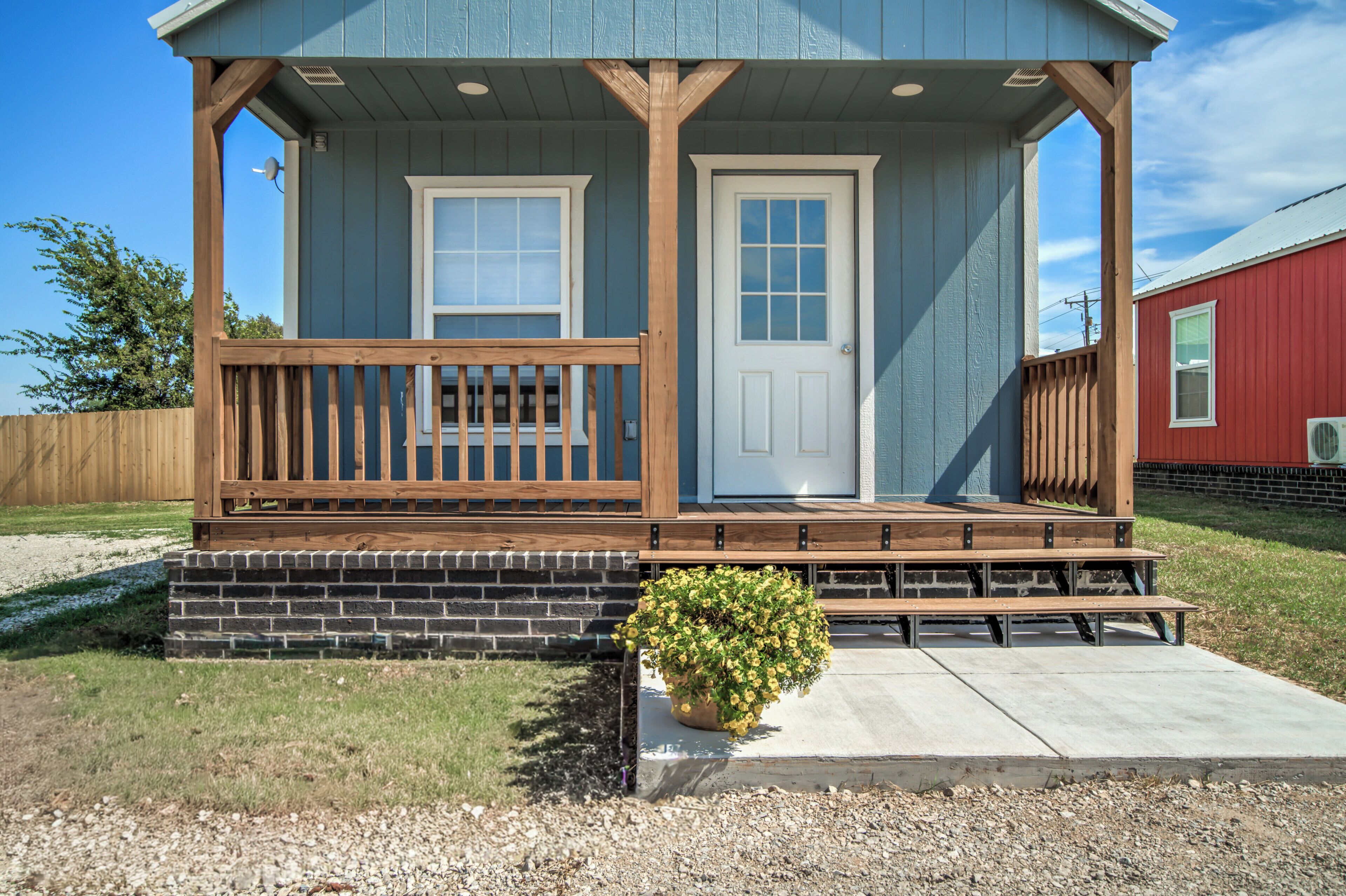 A small house with a porch, two doors, a small garden, and a gravel driveway.